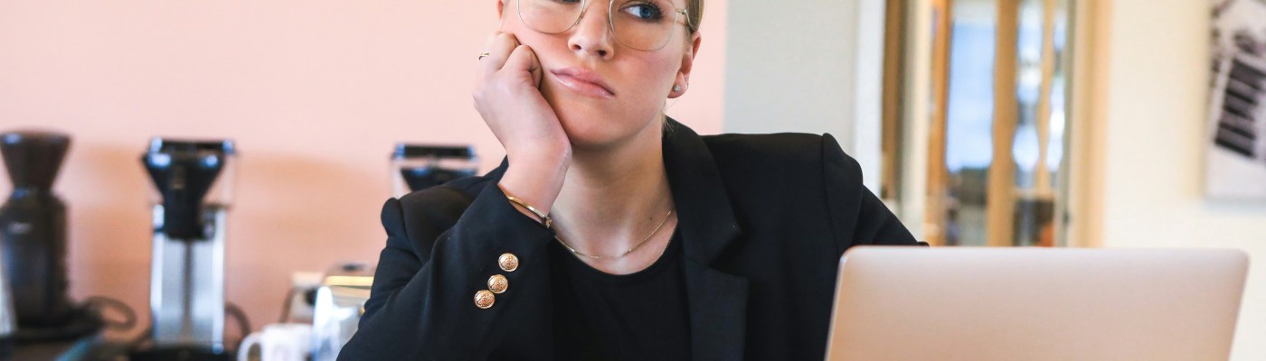 A person sitting at a desk looking a little sad with a laptop and cup of coffee. Photo by Magnet.me, Unsplash