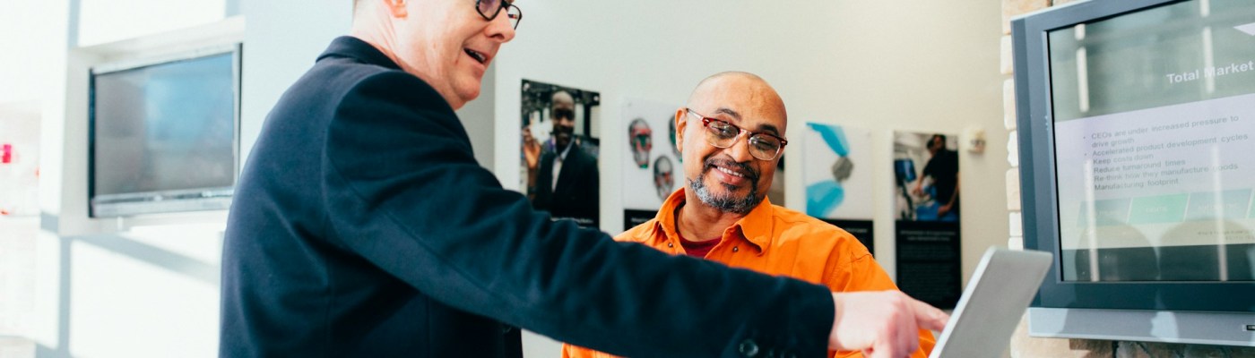 Two people standing and talking while one them points to a laptop