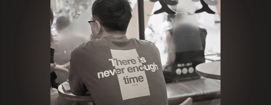 A person sitting with his back to the viewer in a t-shirt that says "there is never enough time"